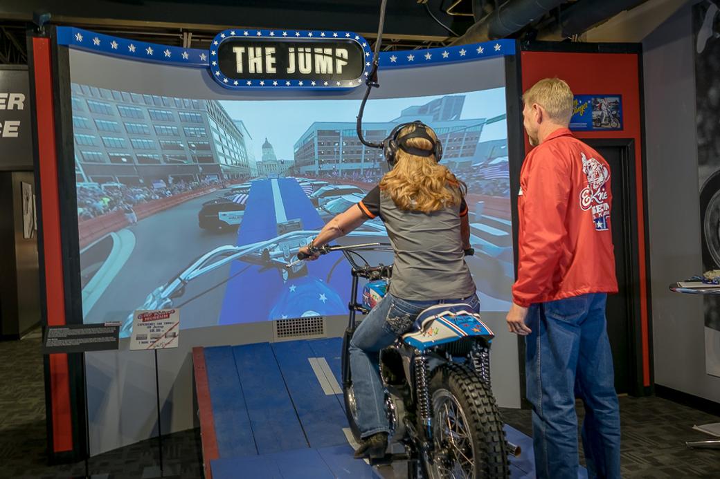 A person on a motorcycle in front of a screen. 