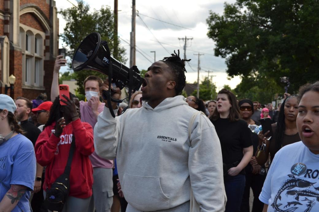 a black man in a gray sweatshirt chants into a megaphone