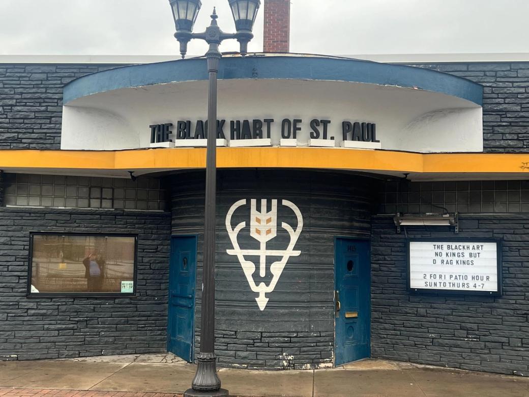 Front exterior of black building with small marquee on cloudy day