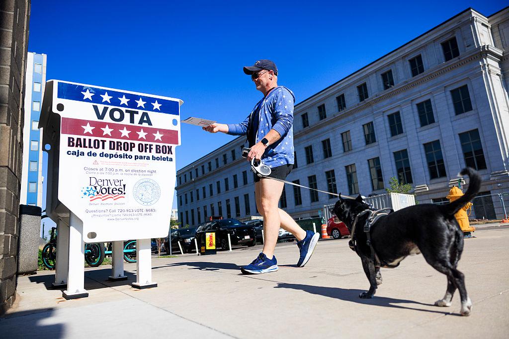 Person with dog drops off a ballot by mail in Denver