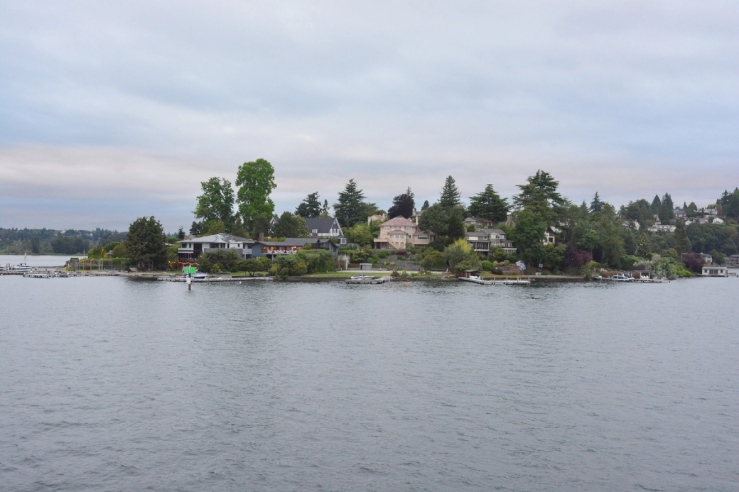 A photo of the Laurelhurst neighborhood taken from a boat on Lake Union in early evening. About four large houses are visible with lawns leading down to the waterfront and a dock on the left hand side.