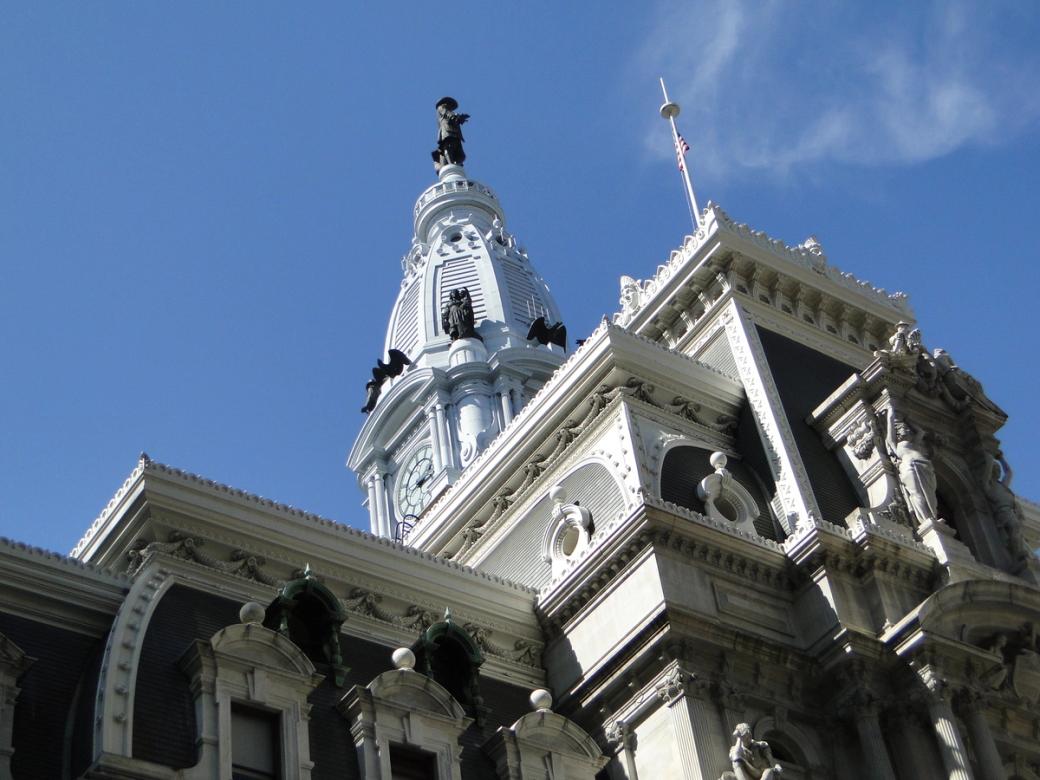 Exterior shot of the top of Philadelphia’s City Hall, designed in the French Second Empire style with brick, white marble, and limestone. Several statues adorn the building, including one of William Penn at the top of City Hall. 