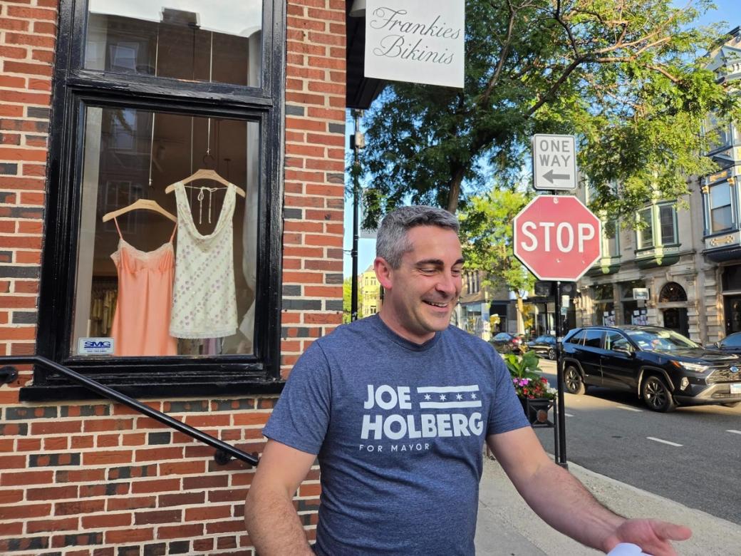 A man in front of a building with a shirt that reads "Joe Holberg"