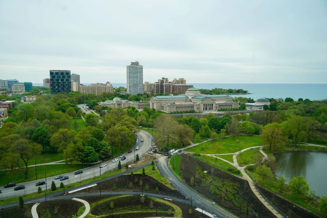 An aerial view of jackson park from the obama presidential center. There are large full trees and roads separating parts of the park