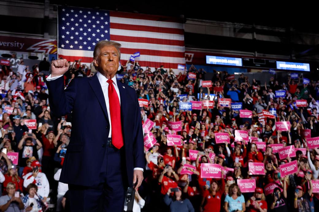 Donald Trump holding up his fist infront of a crowd and American flag