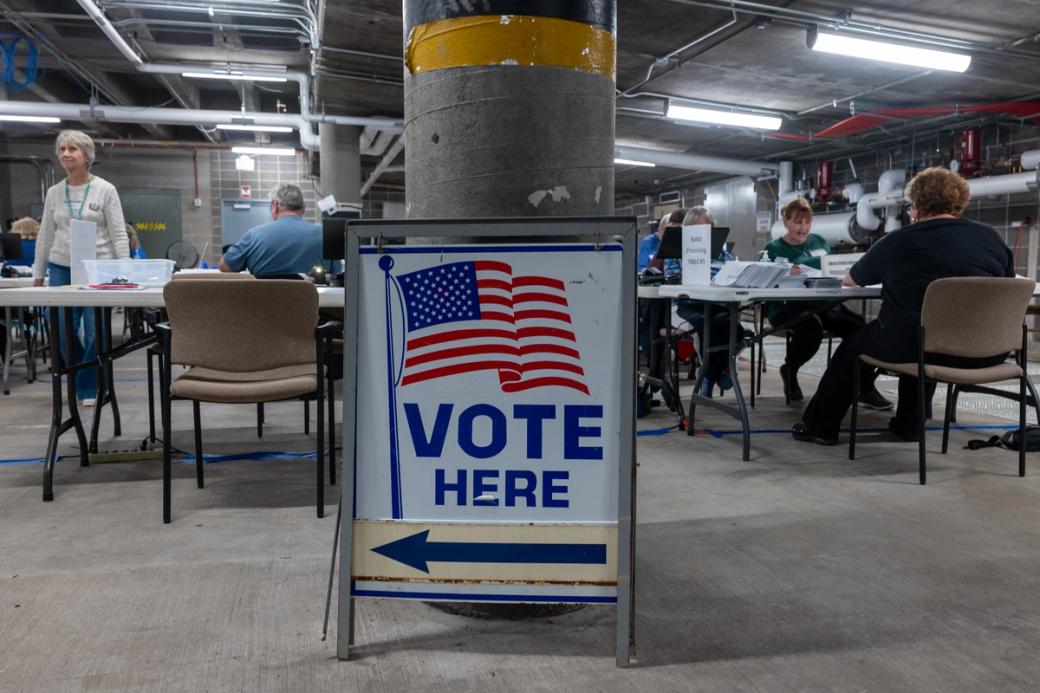 A sign says “Vote Here” in a concrete basement where poll workers sort ballots.