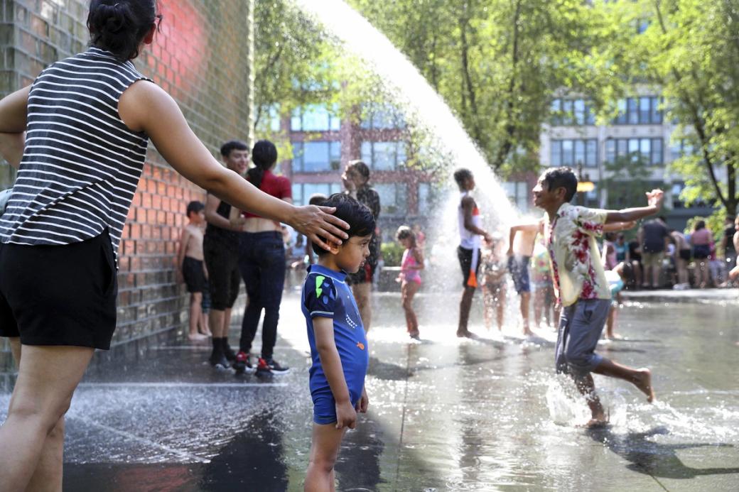 A group of people playing in a fountain. There's a boy with his mother in the foreground
