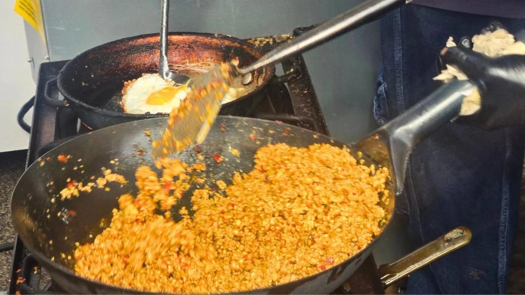 Two pans on a stove. The one in the foreground is a fried rice being tended to. The one in the back is a fried egg