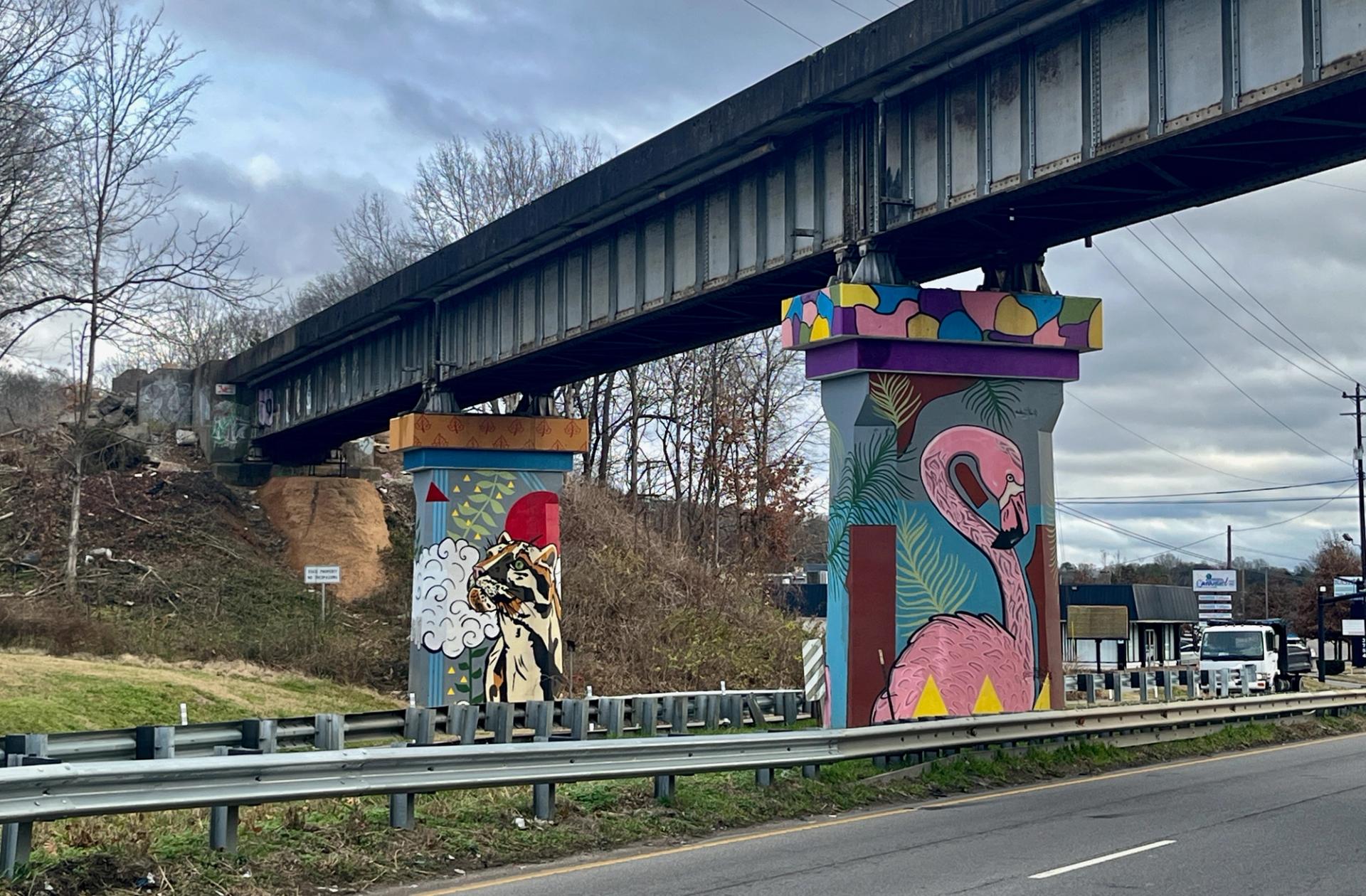 A street with a train bridge over it with murals of a swan and clouded leopard on it.