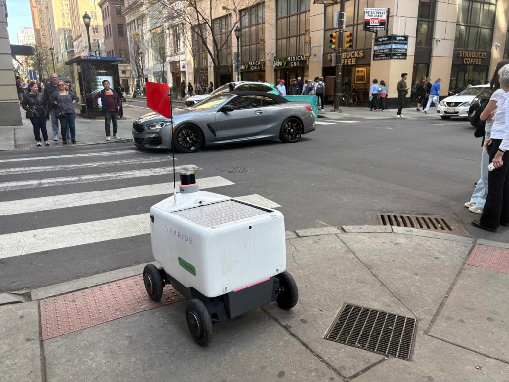 A white delivery robot waits to use a crosswalk in Center City