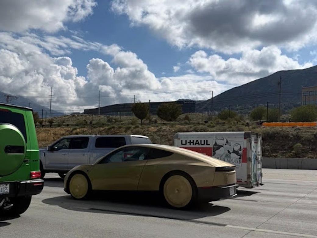 A gold Tesla Cybercab on the freeway with other cars driving nearby. 
