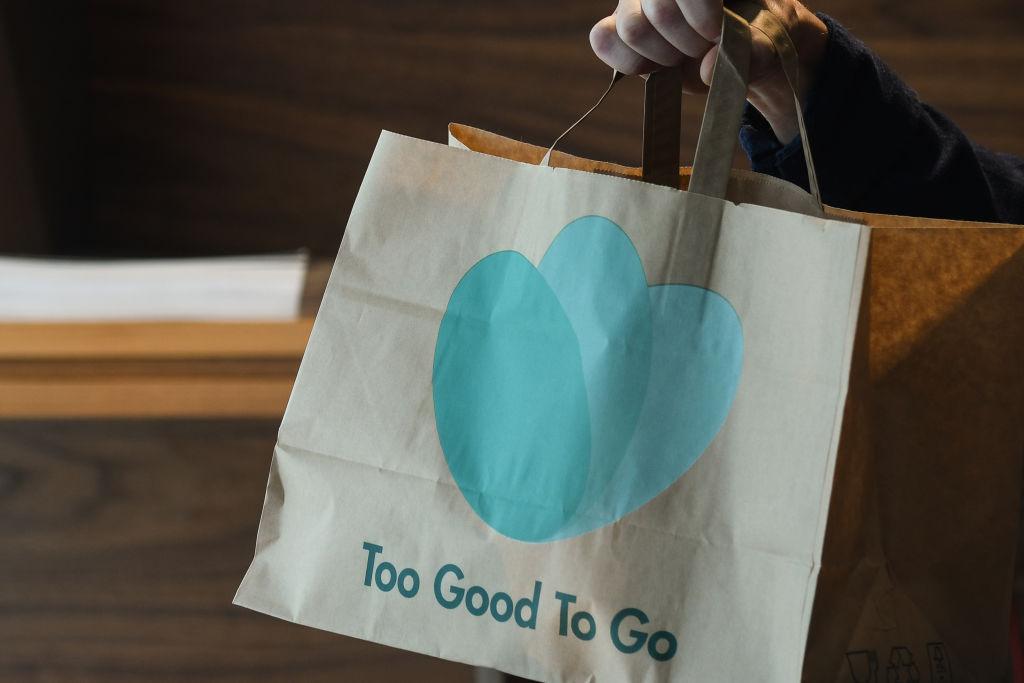 A hand holds a bag that reads "Too Good To Go"