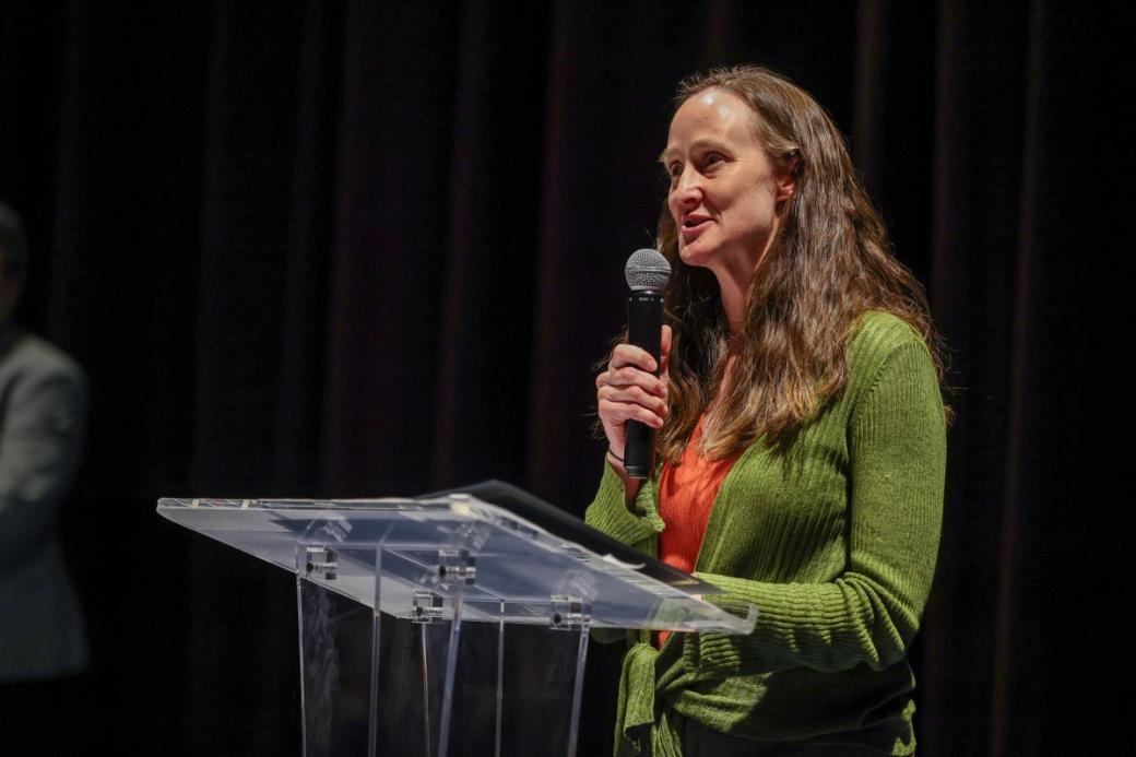 A photo of Katie Wilson speaking with a microphone in front of a podium