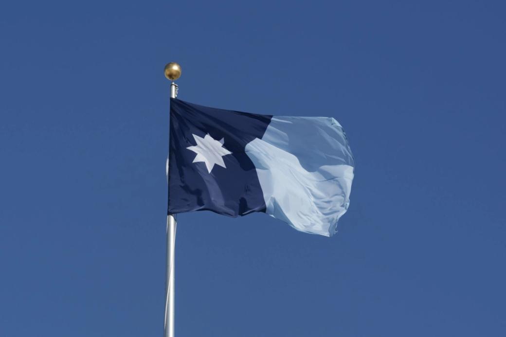 Minnesota state flag on flagpole, blowing in the wind with clear blue skies in the background
