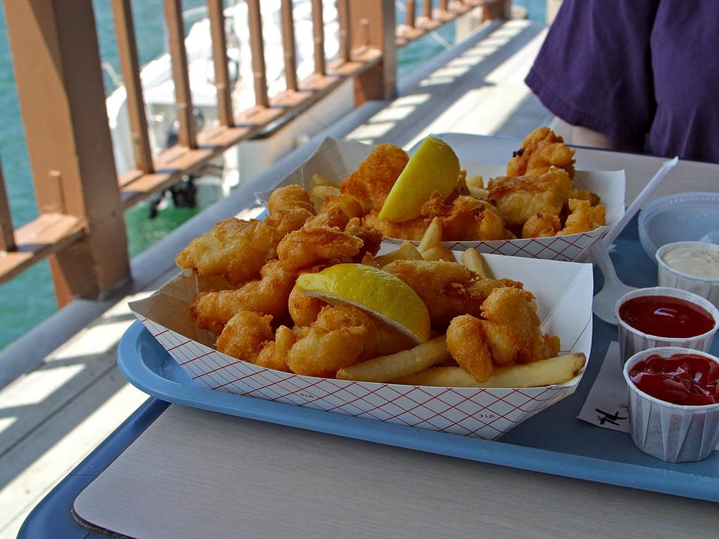Two plastic trays with fried fish and French fries on an outdoor table.