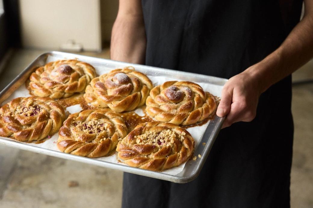 6 pastries on a metal tray held by a person wearing all black