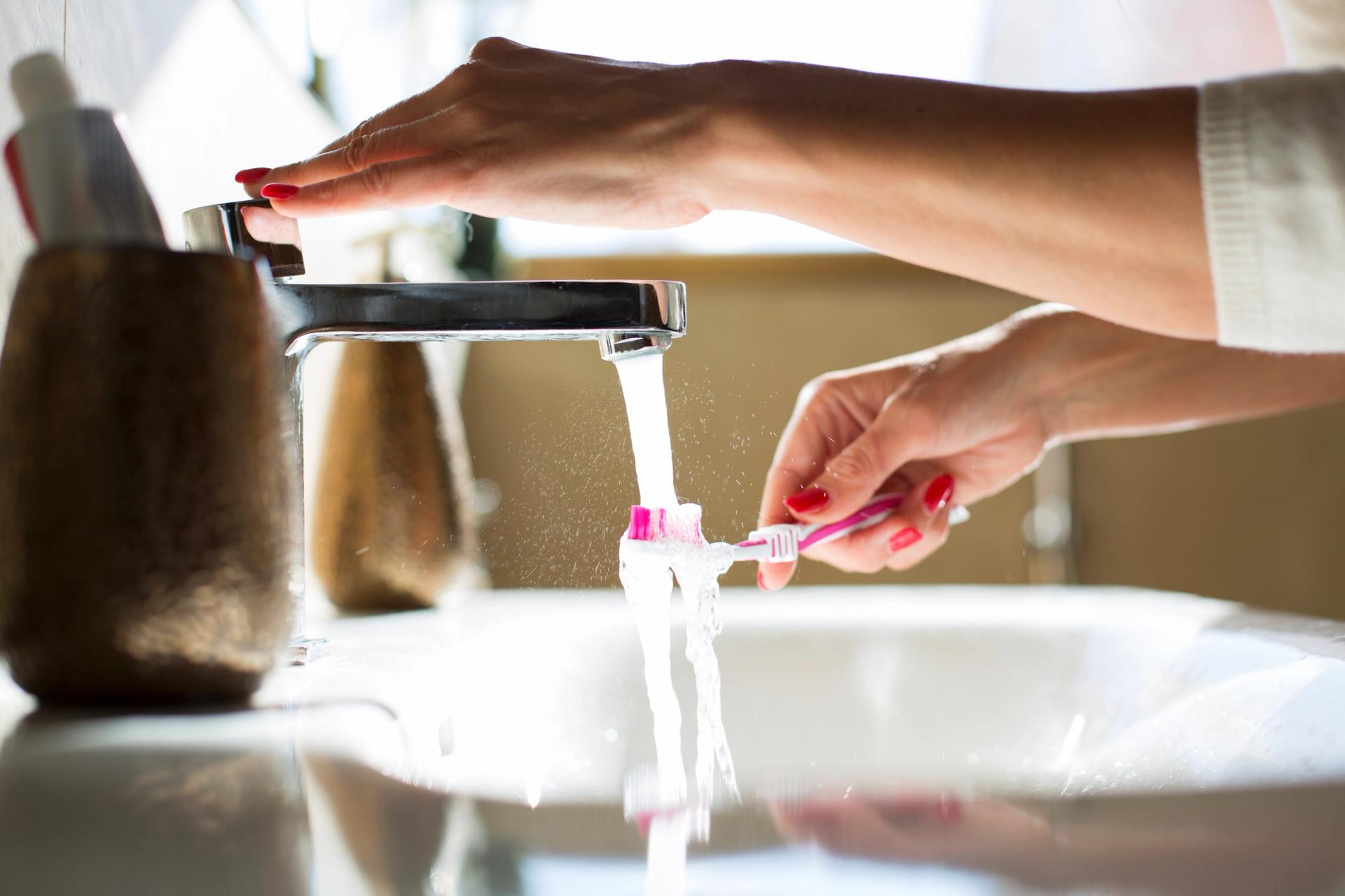 A woman rinses her toothbrush at the sink