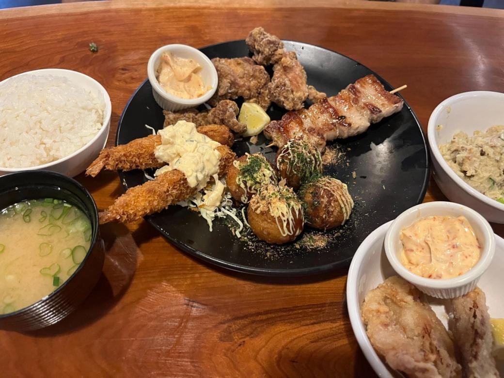 Various plates and bowls with food set out on a table, including fried shrimp and rice and soup
