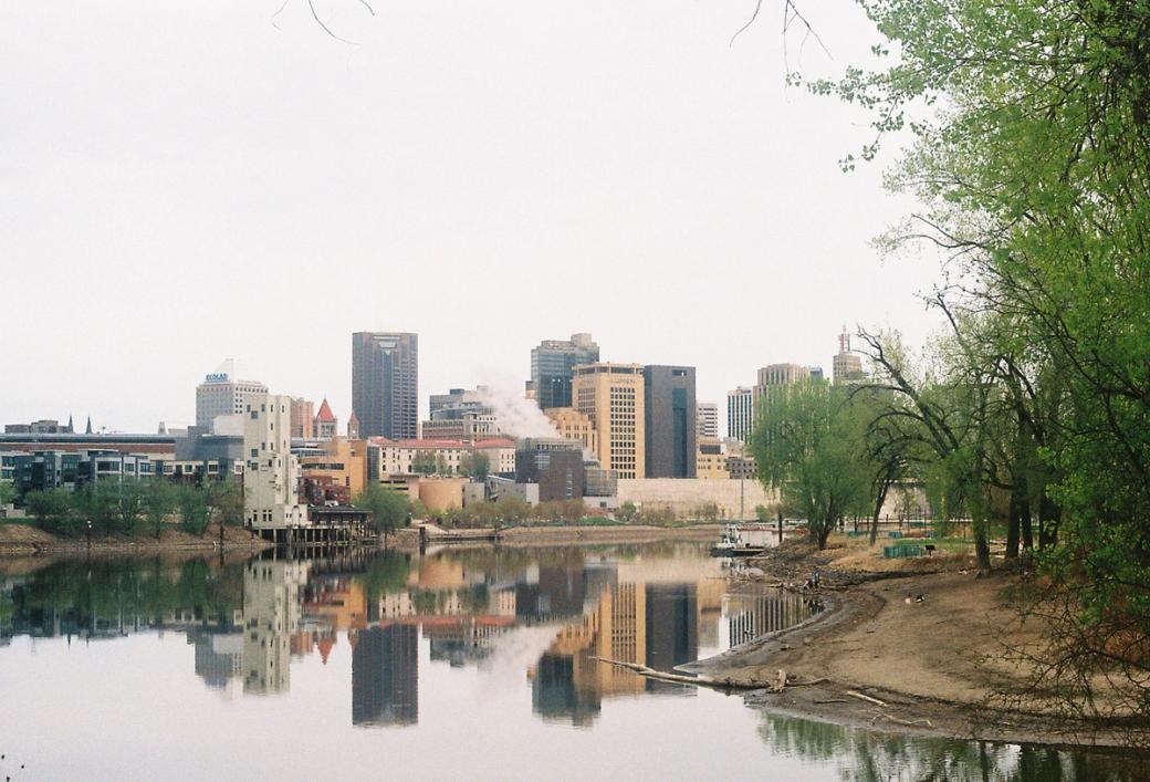 The St. Paul skyline is reflected off a calm Mississippi River on a cloudy day.