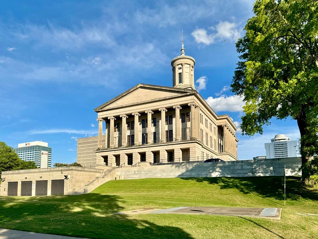 Tennessee's state capitol building on top of a grassy hill. It has columns and is built in the Greek style.