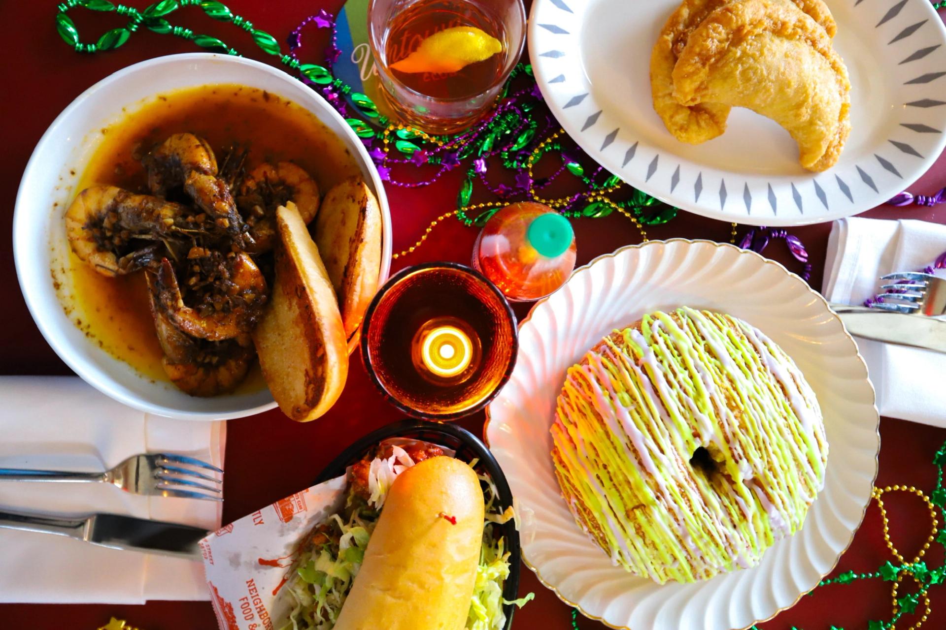An overhead view of a King Cake, a po-boy sandwich, shrimp, and colorful drinks.