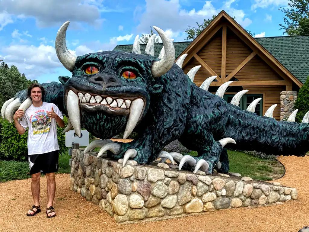 A man in a white shirt next to a giant green statue of a monster.