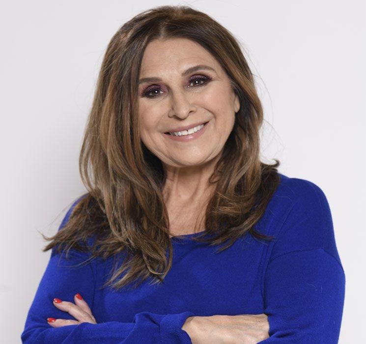 Picture of a woman with long brown hair, wearing a blue shirt, with arms crossed, smiling at the camera.