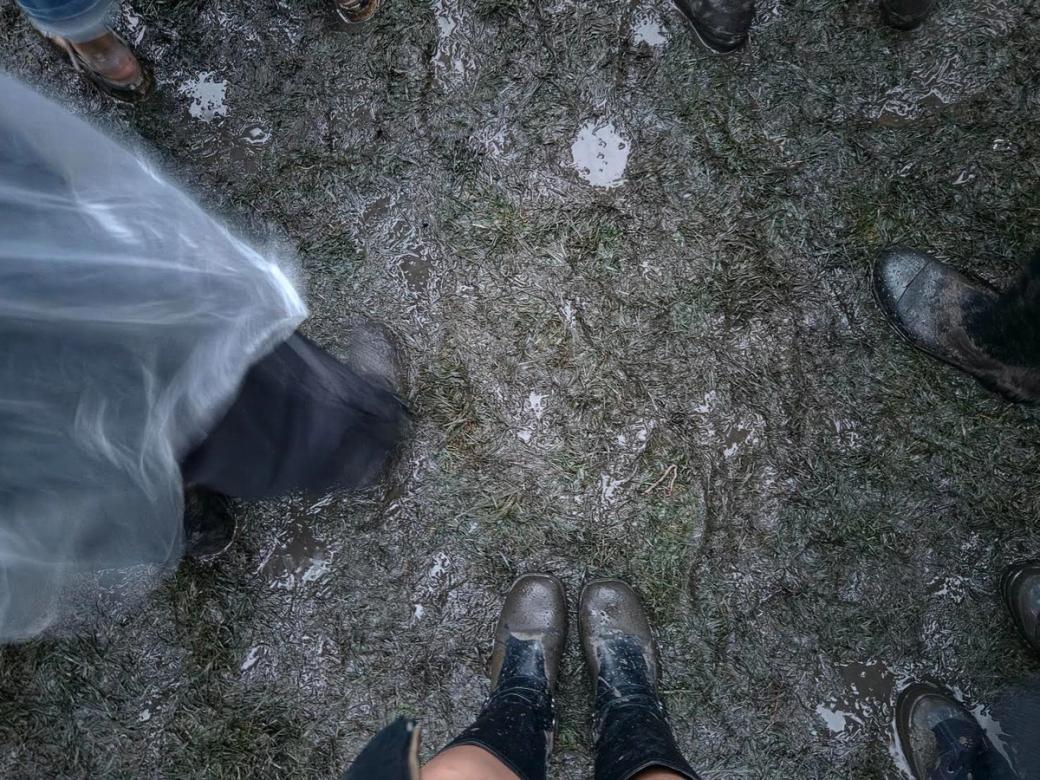 A top down view of people's feet. People are standing in a circle on a muddy ground