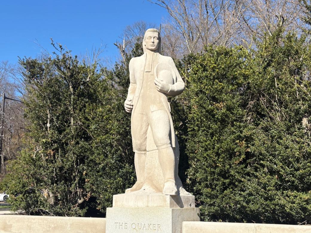 Limestone sculpture of a Quaker man in a park setting
