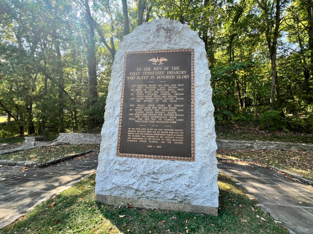 A stone memorial with a dark brown plaque in the woods.
