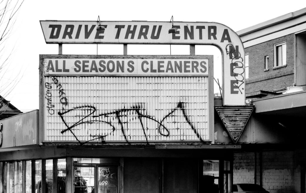 A storefront sign reading “Drive Thru Entrance” and “All Seasons Cleaner” is tagged in several places above a closed business.