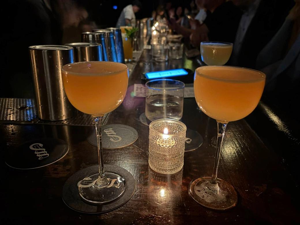 Two cocktails filled to the top by candlelight on a bar