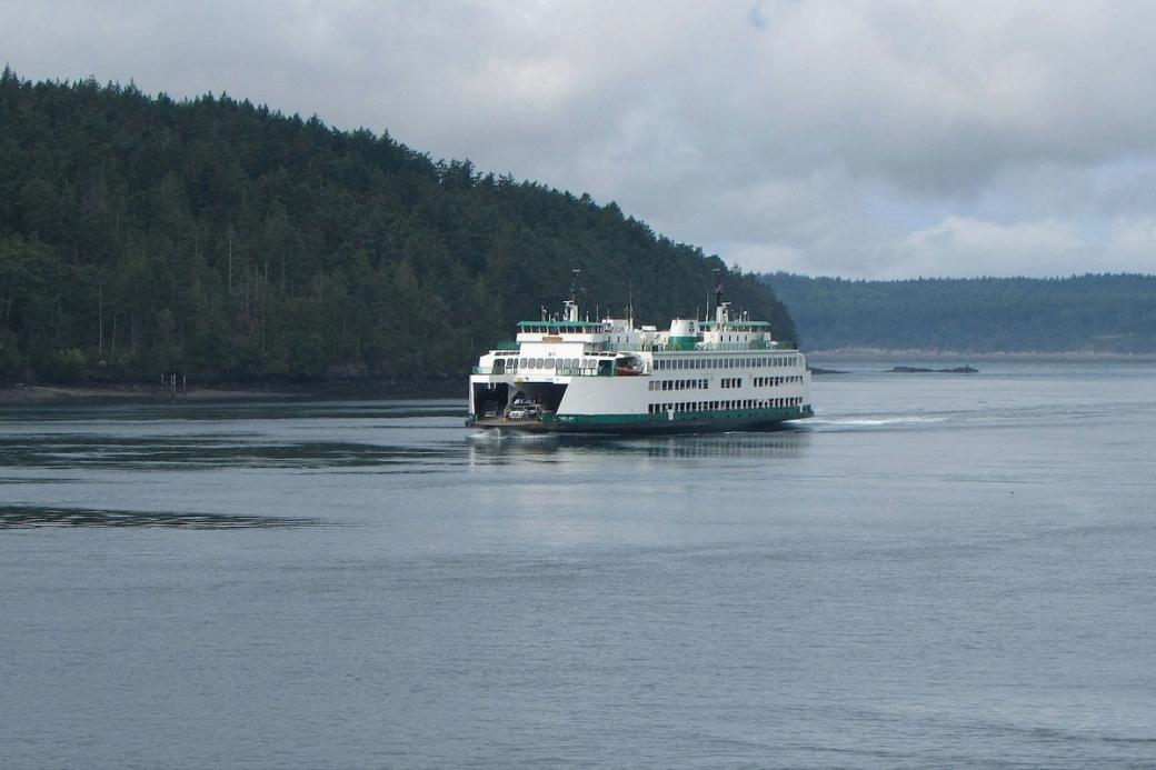 A ship on a pool of water passes greenery during a slightly cloudy day. 
