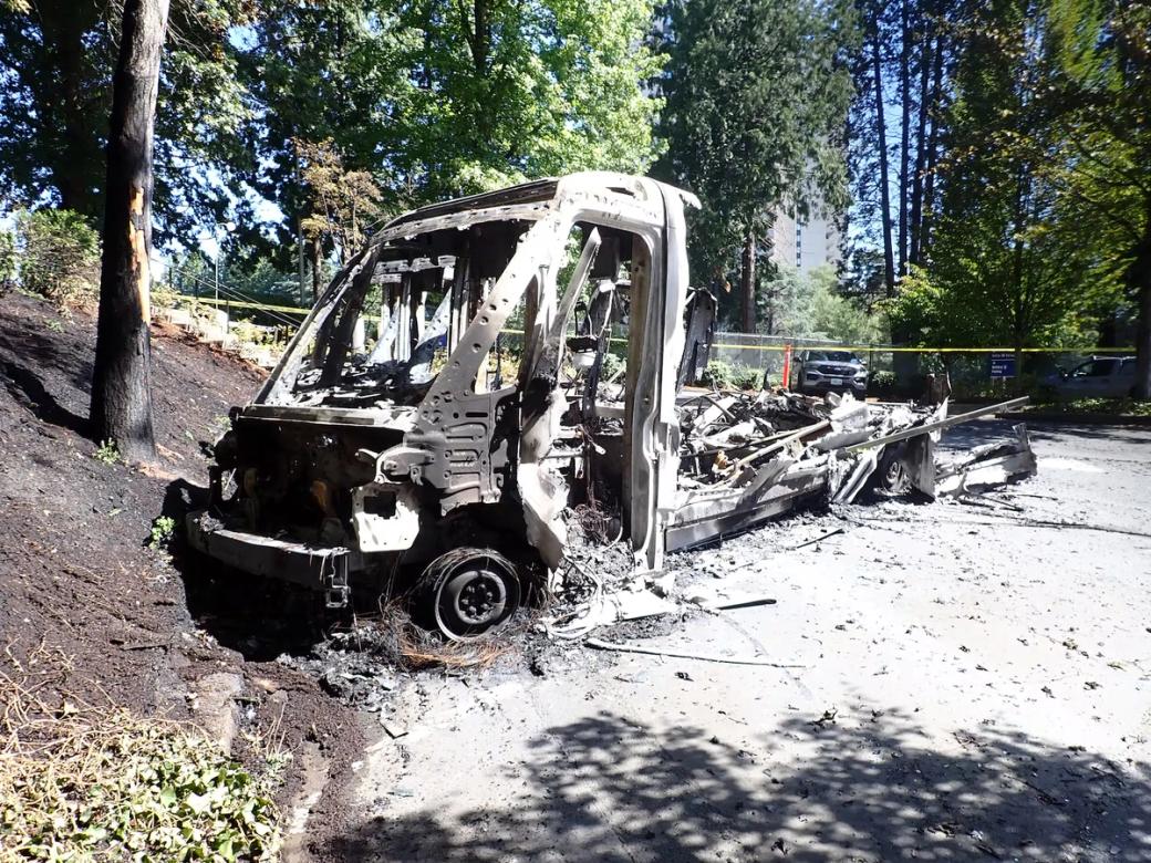 Badly burned delivery truck sits on side of road in wooded area