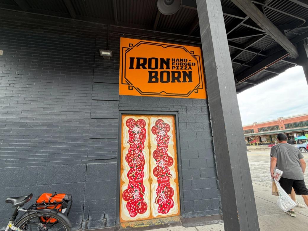 Double doors painted like pizza with toppings. Above them is an orange sign for “Iron Born Hand-forged pizza.”