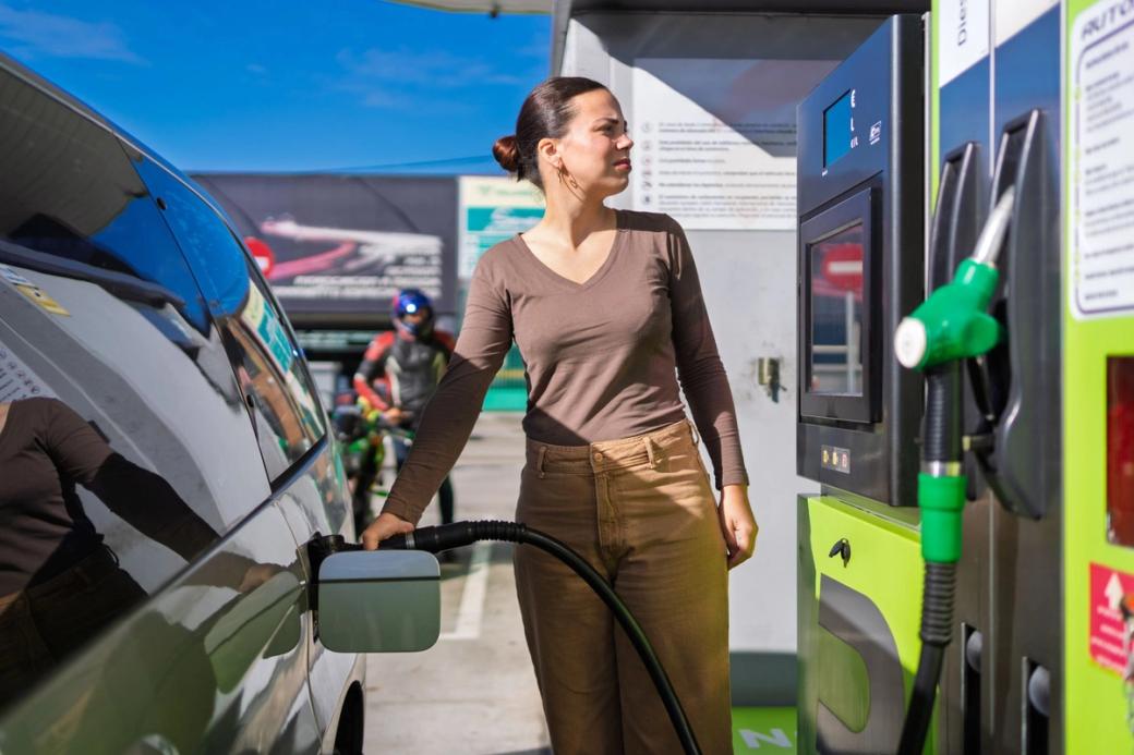 Woman contemplating rising gas prices and environmental impact while refueling car on sunny day
