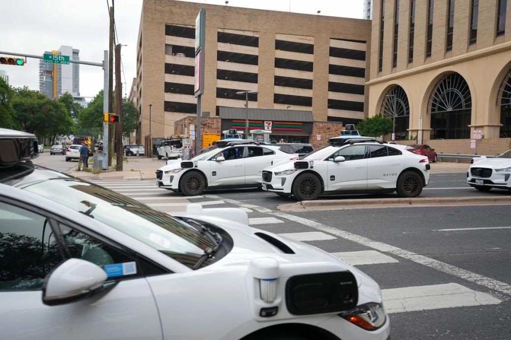 Four white, driverless vehicles at a downtown intersection.