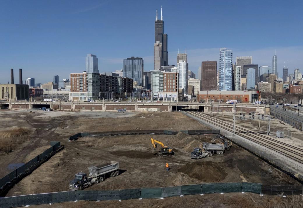 A large plot of land with construction vehicles on it. In the background the Chicago Skyline is visible