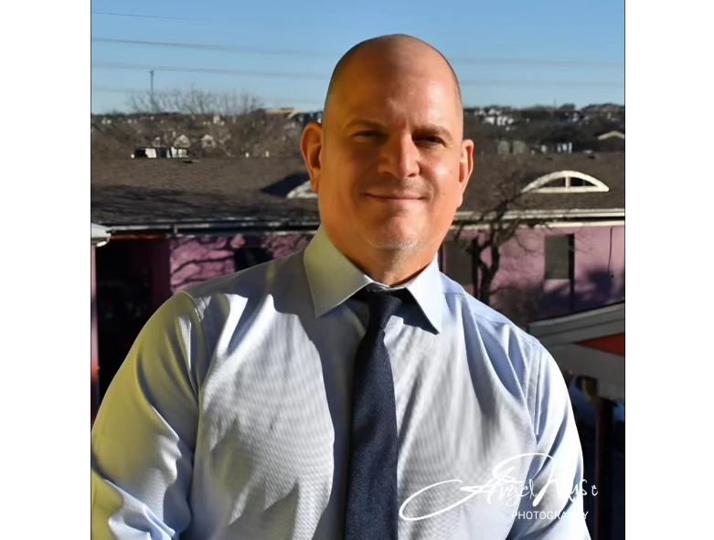 A bald man wearing a light blue button down shirt with a navy blue tie.