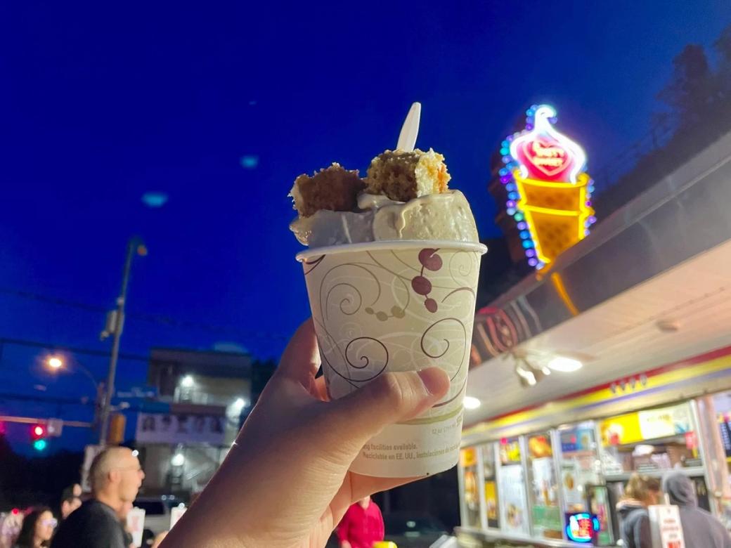 A cup of ice cream with toppings held up before the neon Page's Dairy Mart sign in South Side.