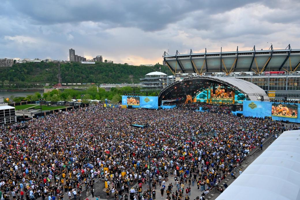 A large crowd of people stands in front of the NFL draft stage