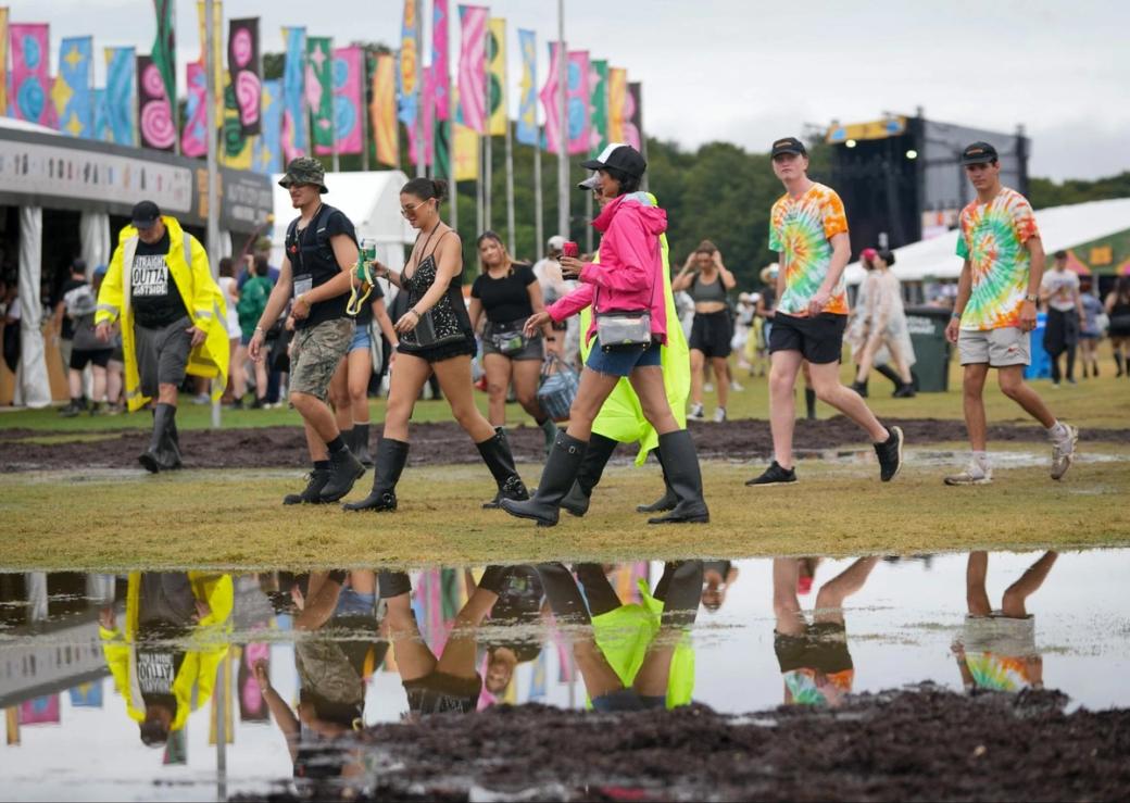 People in rain boots walking across a field near a large puddle.