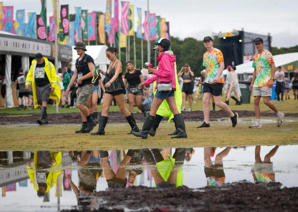 People in rain boots walking across a field near a large puddle.