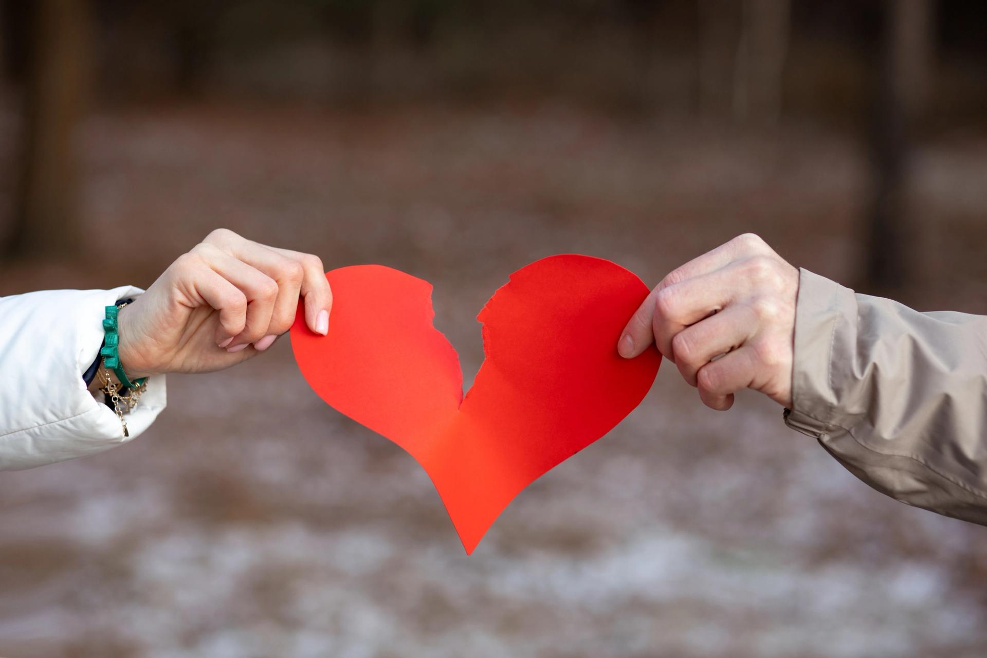 Photo of two hands tearing a paper heart.