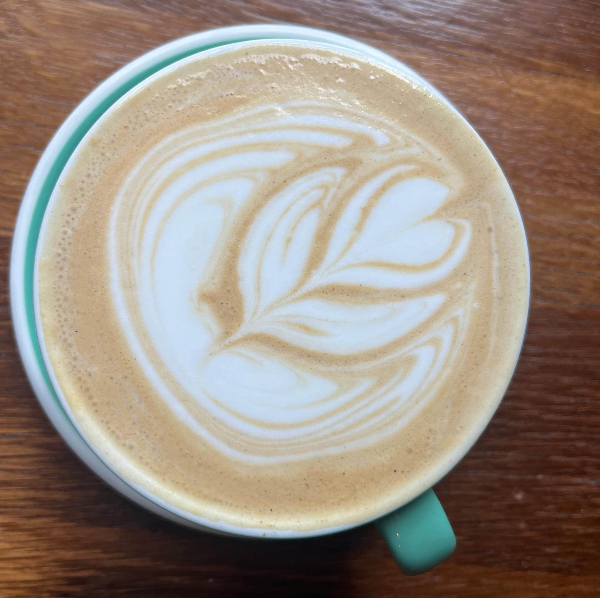 An overhead view of a latte with a bold tulip-shaped milk art design in a mint green ceramic mug on a wooden surface.