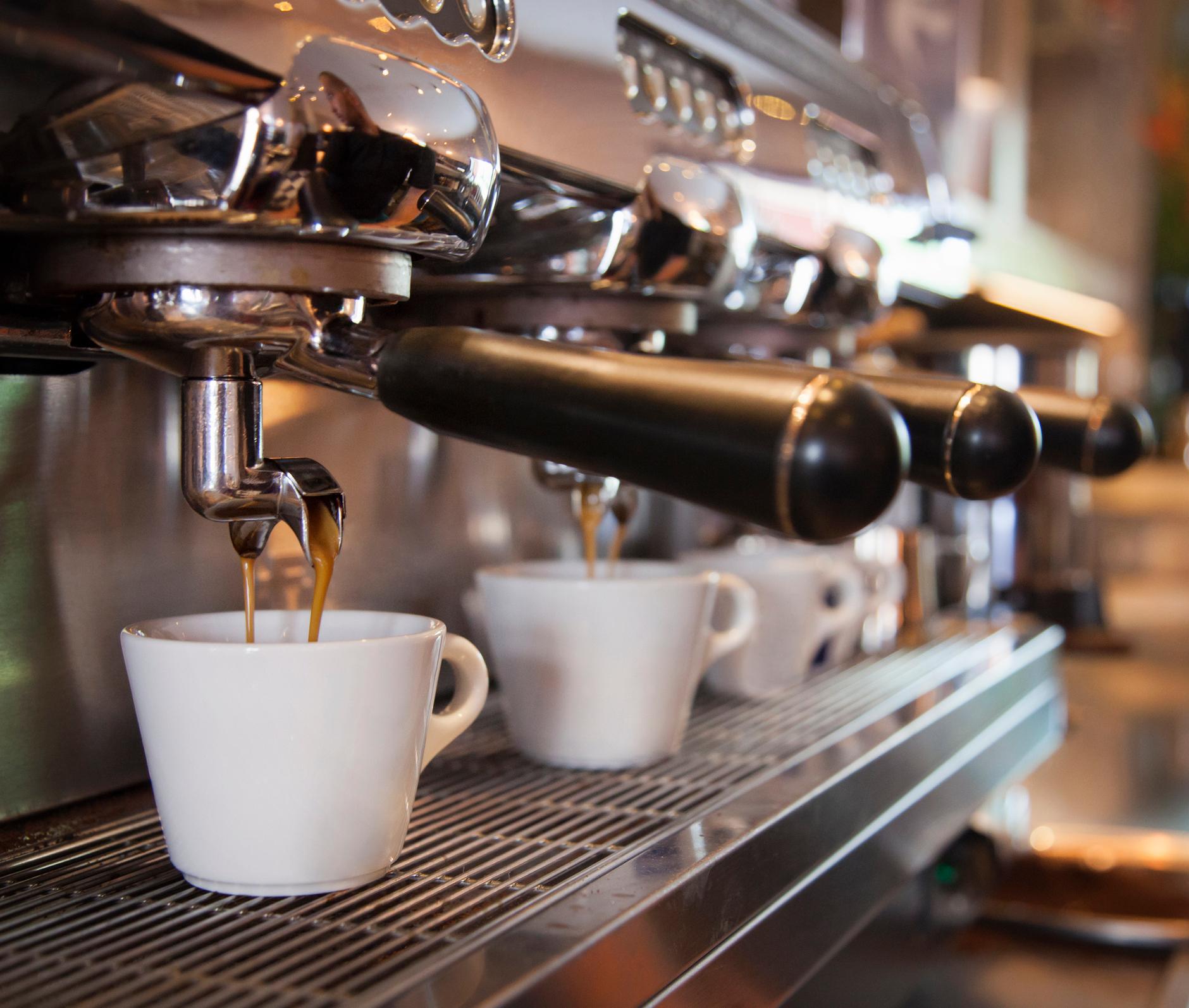 A line of white cups sit in an espresso machine, with espresso dripping down into them.
