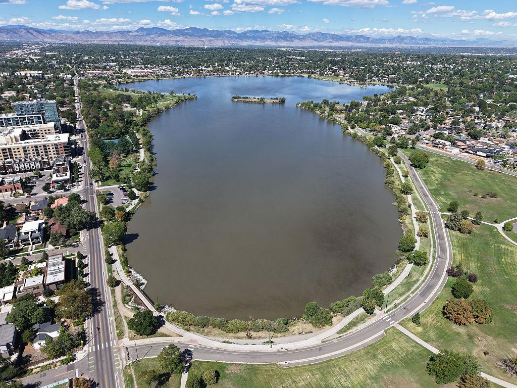 An aerial view of Sloan’s Lake in Denver photographed in September, surrounded by tree-lined residential neighborhoods. The lake is murky brown from decades of sediment buildup.