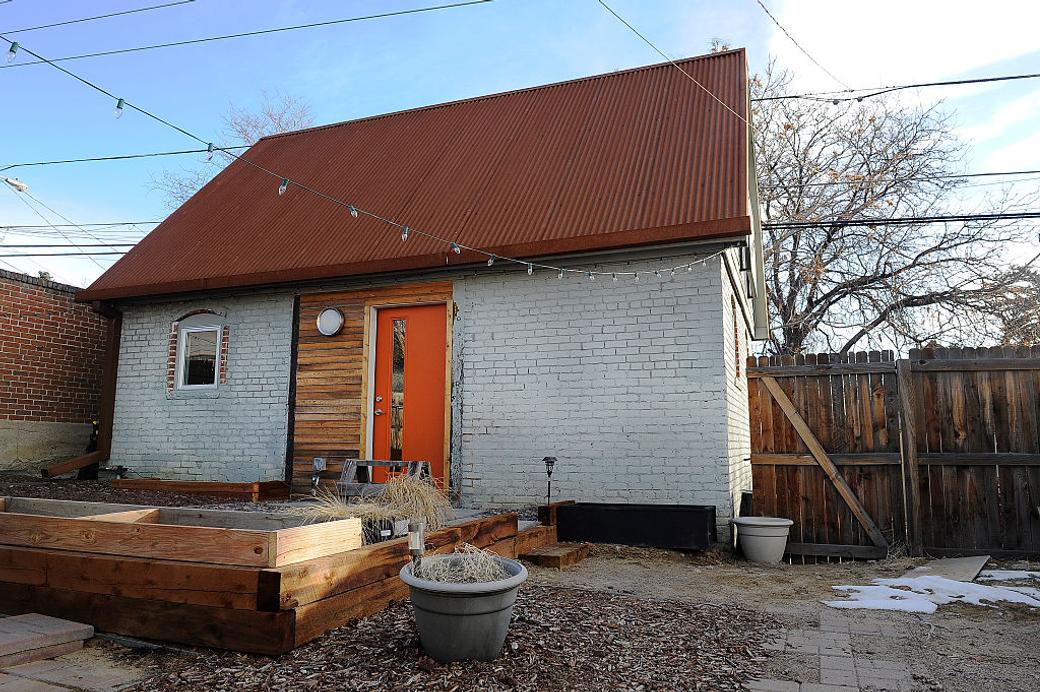 Gray brick house in the back of a property with a rust roof and blue sky