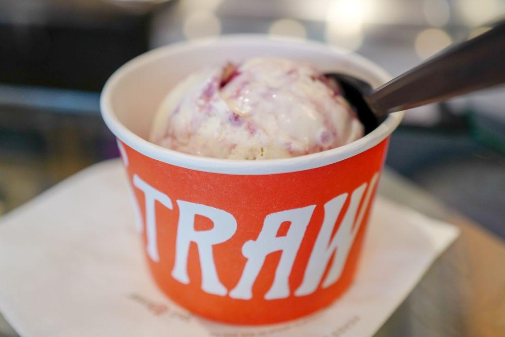A delicious scoop of ice cream nestled inside an orange cup, spoon ever so softly placed in it.