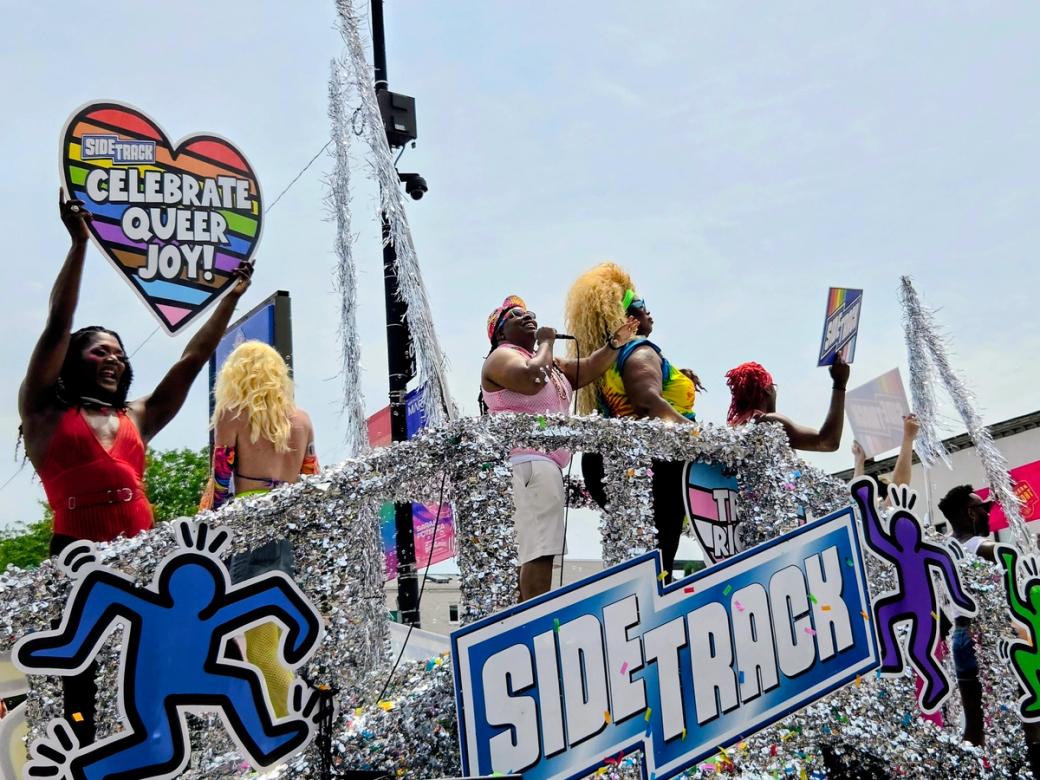 A group of people on a parade float that looks to be bedazzled. The float has a sign that says "sidetrack" Someone is holding a sign that says "celebrate queer joy!"